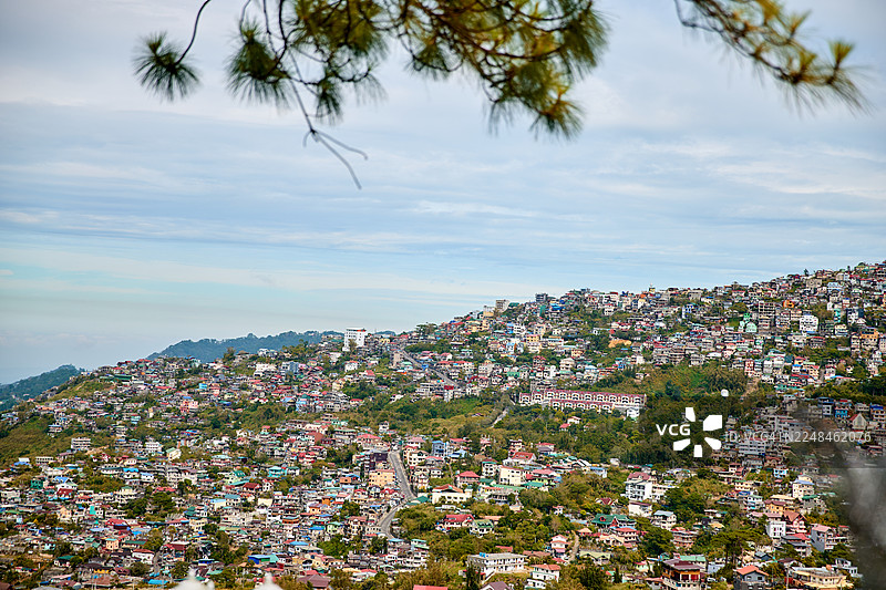 多云天空下，人口密集的山坡城镇。图片素材