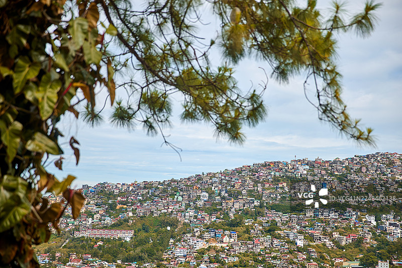 多云天空下，人口稠密的が丘陵城镇。图片素材
