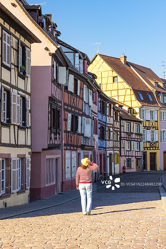 一位游客在美丽的夏日，漫步于科尔马风景如画的村庄小巷中，欣赏着经典的阿尔萨斯风格的立面，科尔马，阿尔萨斯，法国，欧洲图片素材