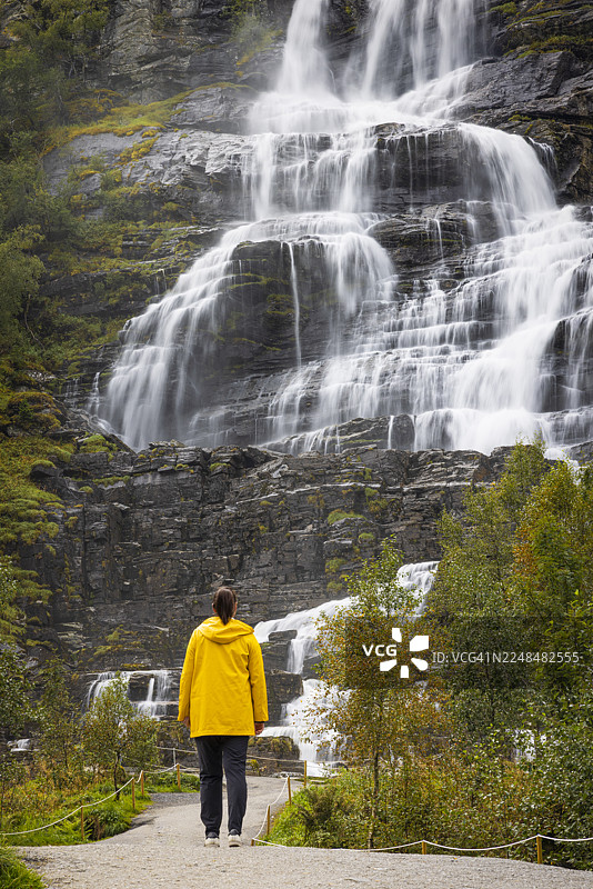 夏日里，一位穿着黄色雨衣的游客在挪威欧洲欣赏特温德瀑布。图片素材