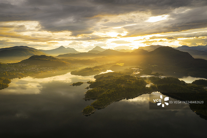 挪威莫尔-奥格-罗姆斯达尔斯科耶，金色日落和远山倒映在平静的湖面上，构成一幅宁静而风景如画的景象，俯瞰视角。图片素材