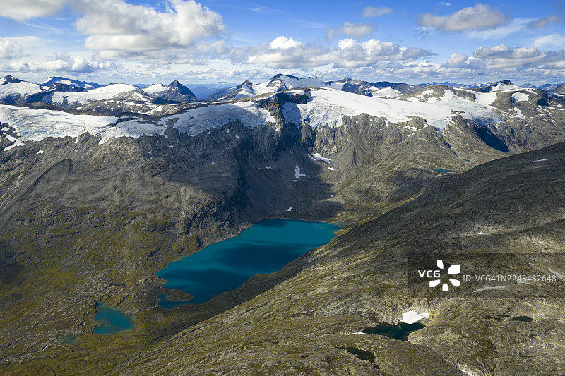 挪威莫勒-鲁姆斯达尔郡盖朗厄尔，一幅生机勃勃的蓝湖坐落于崎岖的雪山之间，明净的天空下，俯瞰视角。图片素材