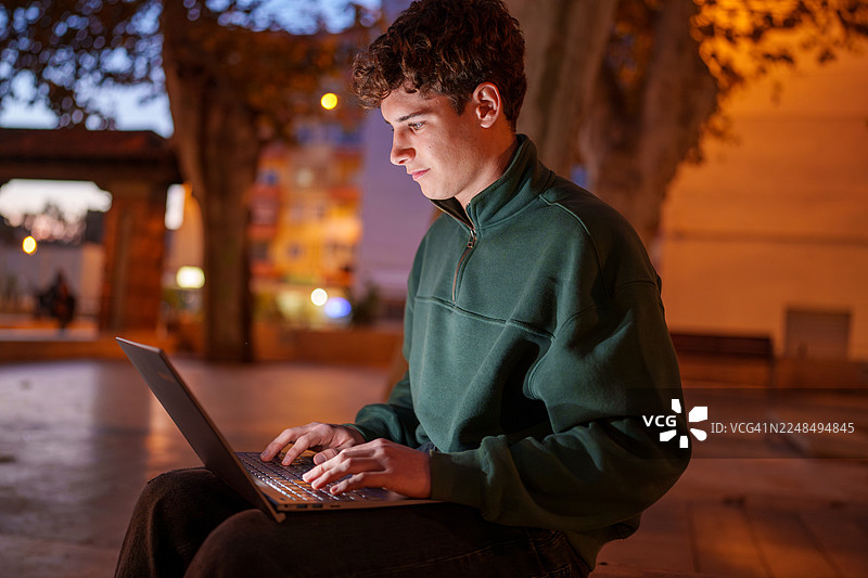少年夜晚在户外使用笔记本电脑工作图片素材