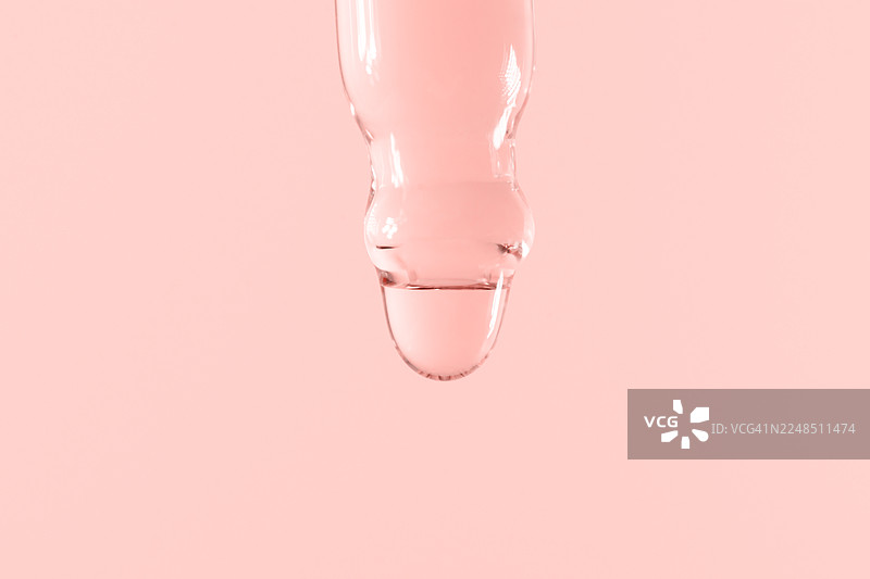 浅粉色背景下，透明玻璃滴管滴下蓝绿色液体的特写，适用于健康、科学和养生项目的抽象医学与科学概念图片素材