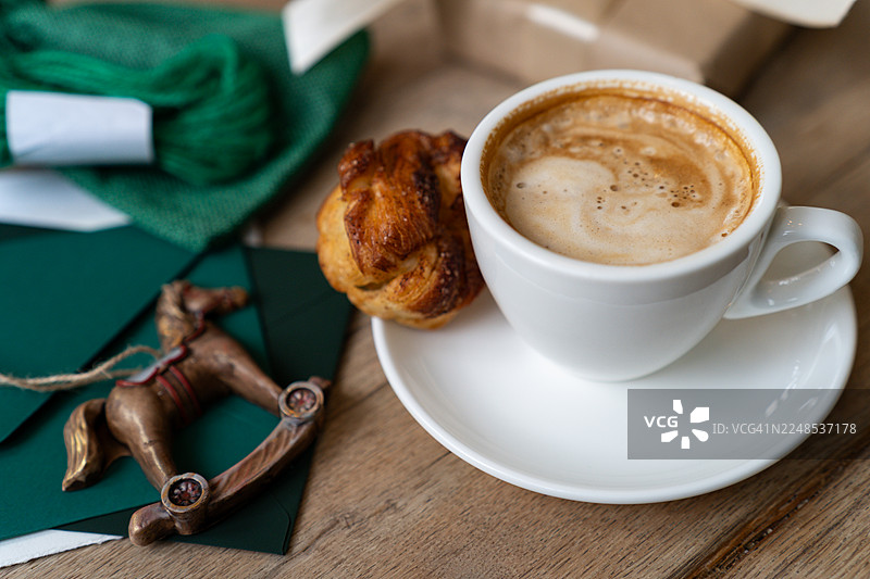 木桌上的一杯咖啡特写，旁边有甜点、摇马装饰、包装好的圣诞礼物和文具图片素材