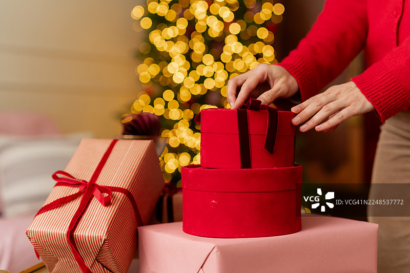 特写：一位女士在亮灯的圣诞树前的客厅里堆叠包装好的圣诞礼物图片素材