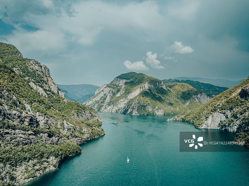 空中影像，展示一艘船在阿尔巴尼亚斯库台县的诅咒山脉科马尼湖上航行图片素材
