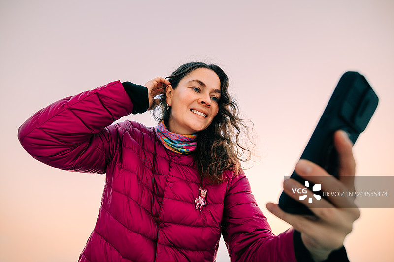 日落时分，一位女士在户外微笑着使用智能手机图片素材