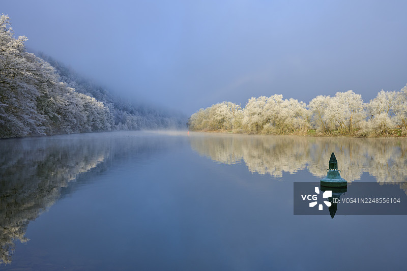 宁静水面上的绿色浮标,周围环绕着雪景、倒映着树木的景象、霜花,这是在德国巴登-符腾堡州美因-陶伯区博克斯塔尔、巴伐利亚州施佩萨特地区米尔滕贝格县的施塔特普罗策尔滕和多夫普罗策尔滕的冬季景象。图片素材