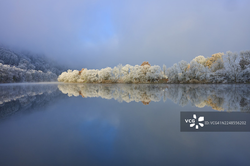 冬日里,在晴朗寒冷的天空下,冰霜覆盖着树木,镜面般的河流宁静地流淌,这是德国巴登-符腾堡州美因-陶伯区博克斯塔尔、巴伐利亚州施佩萨特地区斯塔特普罗策尔滕和多夫普罗策尔滕的冬日风光。图片素材