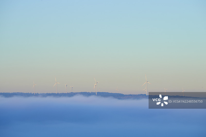 德国巴伐利亚州米尔滕贝格斯佩萨特地区，山丘上的风力发电机，前景是雾，天空是蓝色图片素材