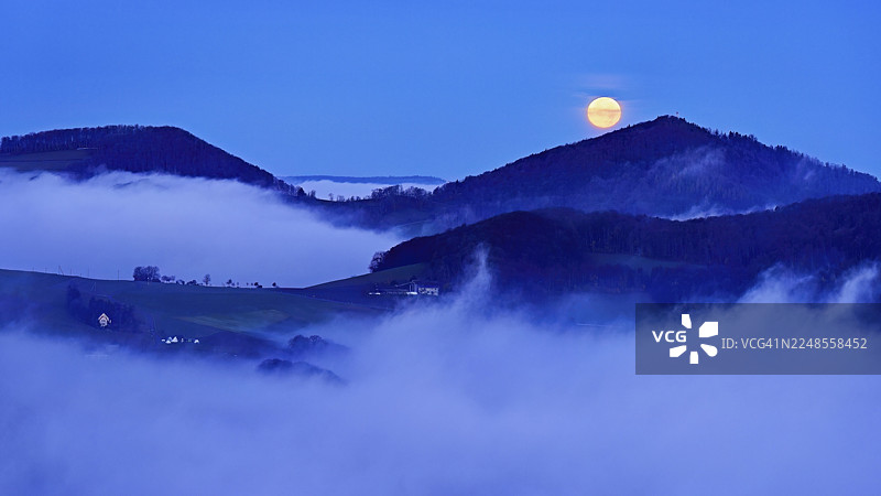 从吉斯利弗卢(Gisliflue)看到的侏罗纪山麓被左侧的雾气笼罩,阿斯佩斯特里亨(Asperstrihen)、施特里亨(Strihen),在满月的映衬下,塔尔海姆(Talheim),阿尔高州(Canton Aargau),瑞士图片素材