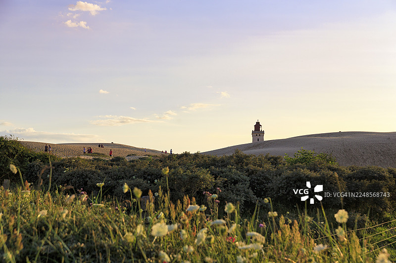 鲁布耶格·克努德灯塔在地平线上，徒步者在沙丘上行走，夏日傍晚的氛围，勒肯，洛肯，北日德兰，丹麦图片素材
