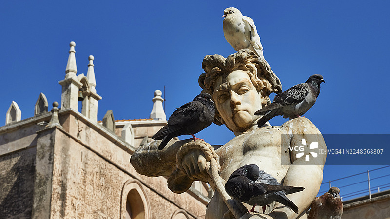 蓝天下的大理石雕塑与鸽子,背景是历史悠久的巴洛克风格建筑,蒙雷阿莱大教堂,联合国教科文组织世界遗产,西西里岛,意大利图片素材