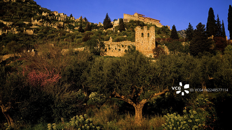 阳光下的城堡遗址，坐落于树木繁茂的山丘上，位于希腊的米斯特拉斯，该地是联合国教科文组织认定的世界遗产，一座中世纪拜占庭风格的废弃城市，位于斯巴达西北部，泰格托斯山脉的余脉，伯罗奔尼撒半岛。图片素材