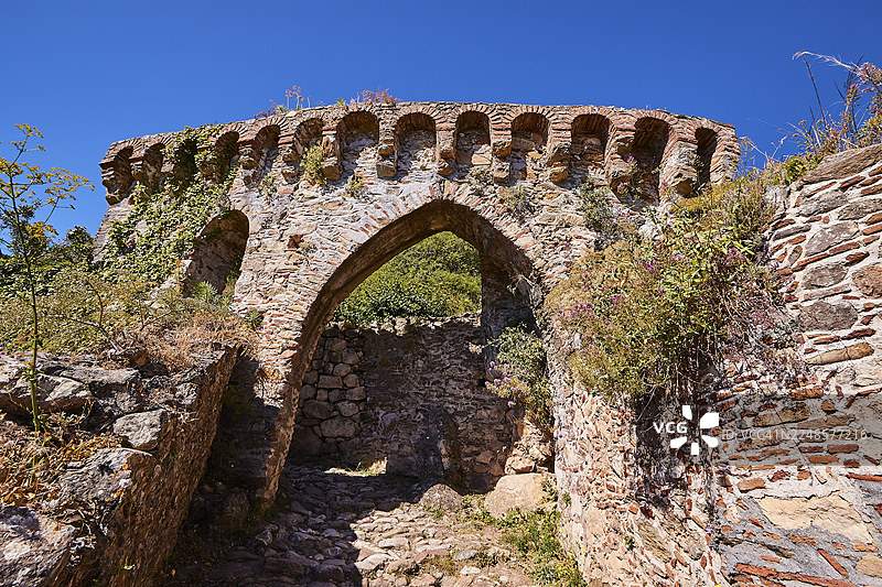 一座宏伟的石头拱门，周围环绕着古老的城墙和野生的植被，位于希腊伯罗奔尼撒半岛，斯巴达西北部，泰格特斯山脉的山麓，米斯特拉斯（又称米斯特拉），一座中世纪拜占庭风格的遗址城市，被列为联合国教科文组织世界遗产。图片素材