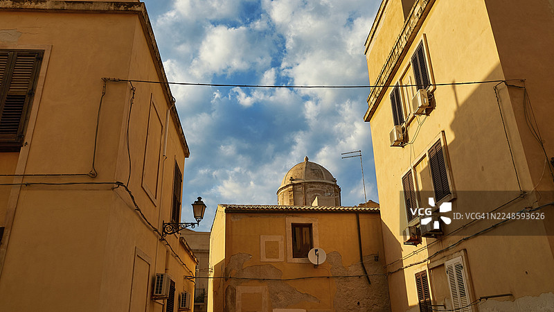从黄色房屋和电缆中看到的圆顶的狭窄视角，背景是部分多云的天空，位于意大利西西里岛锡拉丘兹的奥提伽岛历史中心。图片素材