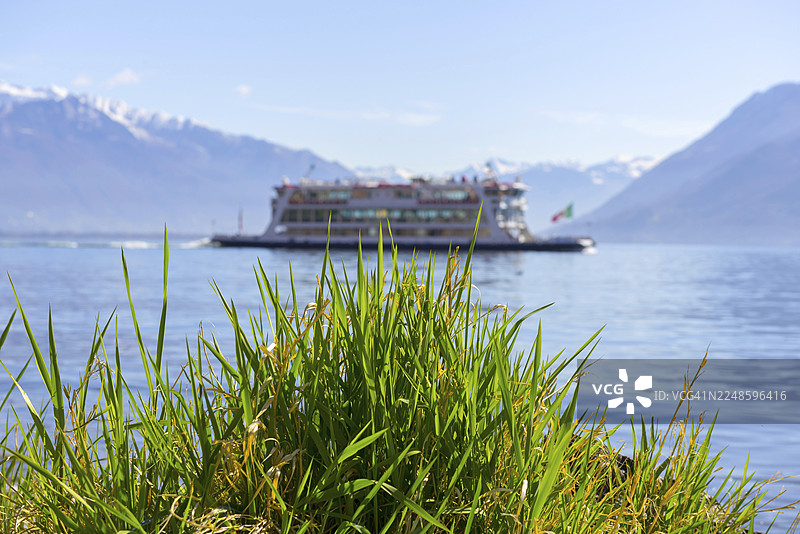 晴天在意大利皮埃蒙特卡诺比奥的马焦雷阿尔卑斯湖上，有雪山和草地的客船图片素材