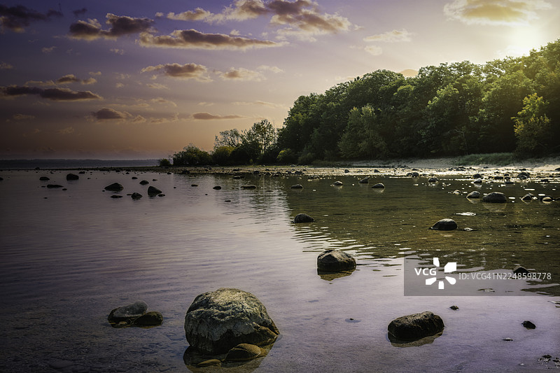 美国特拉弗斯城，生机勃勃的绿树环绕着岩石湖岸，景色宁静的日落图片素材