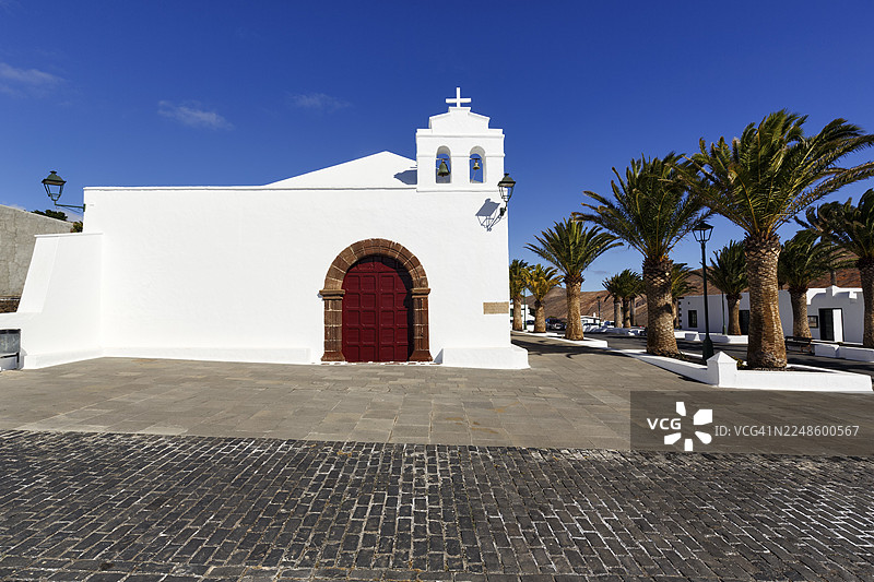 西班牙兰萨罗特岛亚伊萨镇菲梅斯山村的圣马西尔·德·鲁比孔教堂和圣马西尔·德·利摩日礼拜堂旁的教堂广场及棕榈树图片素材