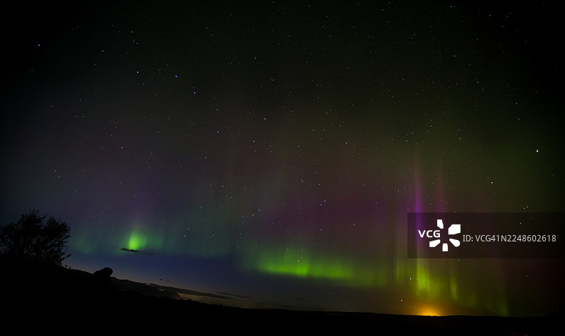 绚丽的北极光以惊艳的绿色和紫色照亮了黑暗的夜空，笼罩着下方漆黑的大地。图片素材
