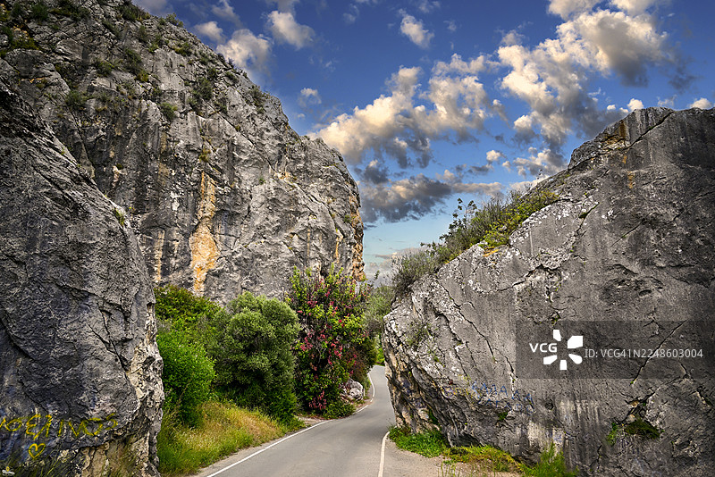蜿蜒的道路穿过崎岖的山隘，天空戏剧性地变化着，塞浦路斯图片素材