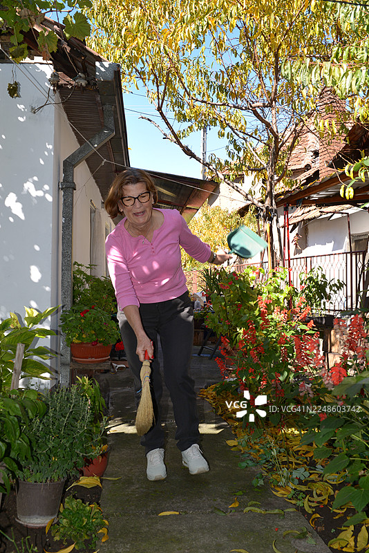 一位女士在她阳光明媚的后院花园里微笑着打扫落叶图片素材