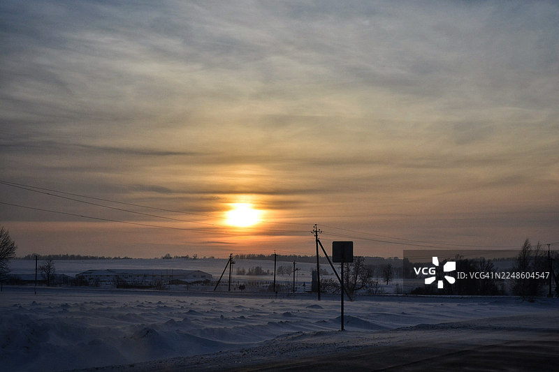 俄罗斯乌法冬季日落，雪地乡村景色，有电线和远处的建筑图片素材