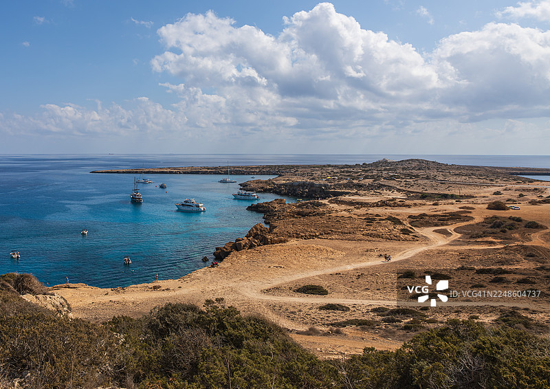 蓝天白云下，风景如画的海湾，停泊着船只，海岸线崎岖，位于塞浦路斯艾依阿纳帕。图片素材