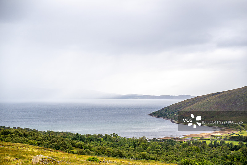 宁静的海边风景，有平静的海面、葱郁的绿色山丘和多云的天空，营造出宁静与自然之美的感觉，英国阿普尔克罗斯图片素材