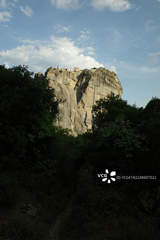 低角度拍摄的梅黛奥拉修道院，它们坐落在高耸的岩石构造之上，背景是蓝天白云，地点在希腊。图片素材