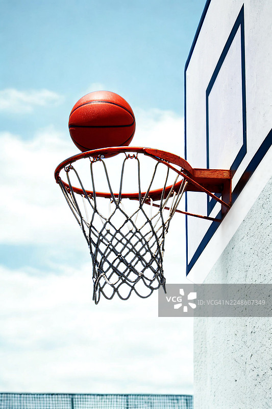 篮球架上的篮球挂在篮筐上，背景是蓝天，象征着体育运动中的擦肩而过或悬念时刻图片素材