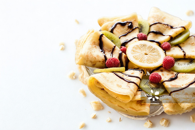 白色背景上的美味可丽饼，配有新鲜水果和巧克力酱，非常适合作为早餐或甜点图片素材