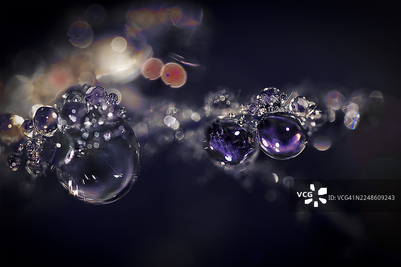 深色背景下闪烁的紫色水滴和散景灯光的特写，营造出抽象而空灵的效果图片素材