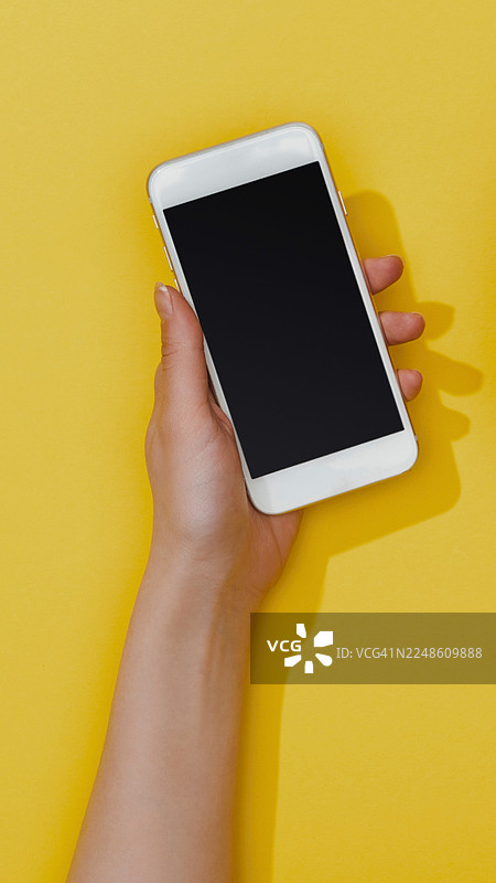 一只手拿着一部白色、屏幕空白的智能手机，背景是鲜艳的黄色图片素材