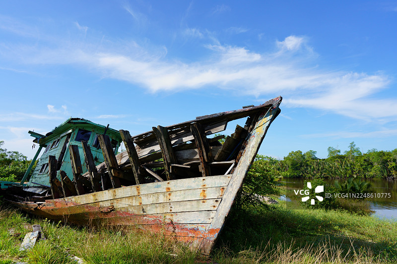 废弃的木船在蓝天下的草岸边腐朽，位于马来西亚的Teluk Kalung, Telaga Simpul图片素材