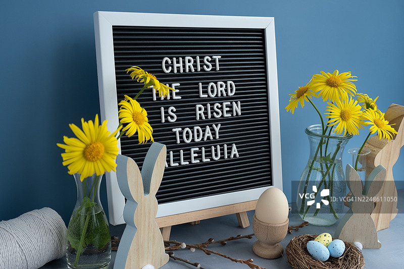复活节装饰，有字母板、黄色花朵和木兔子，摆放在灰色桌子上，背景是蓝色墙壁图片素材