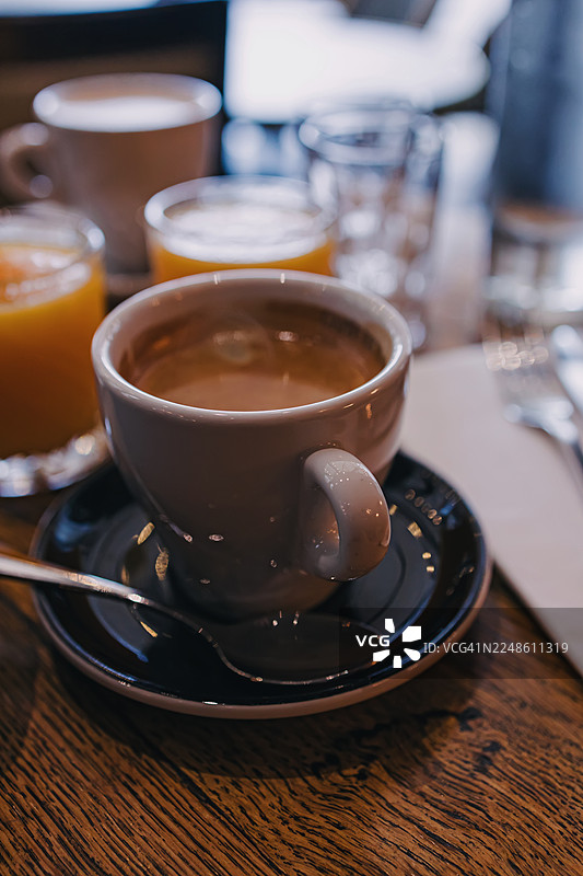 木桌上咖啡杯和碟子的特写，碟子旁放着一把勺子，还有其他饮品。图片素材