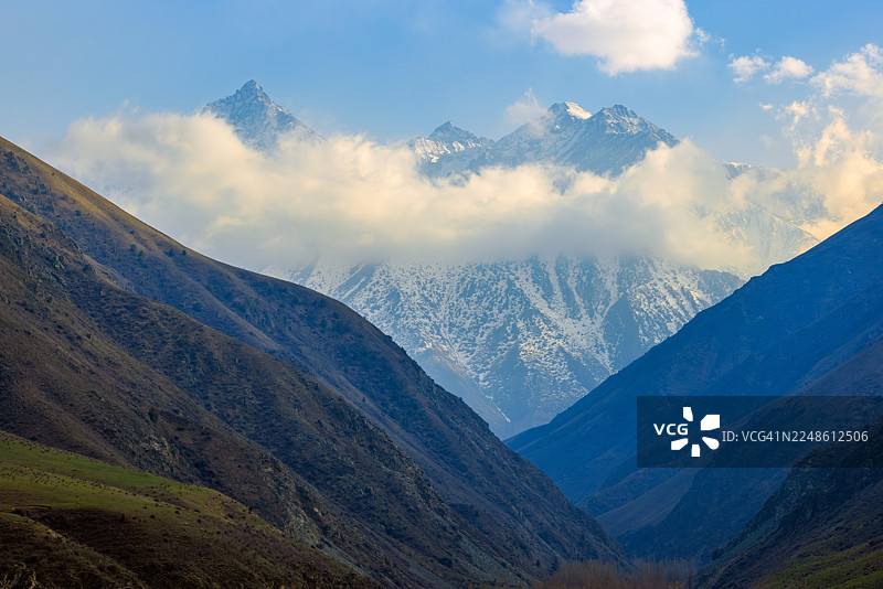 雄伟的雪山在晴朗天空下，穿过云层，被陡峭的山谷环绕图片素材