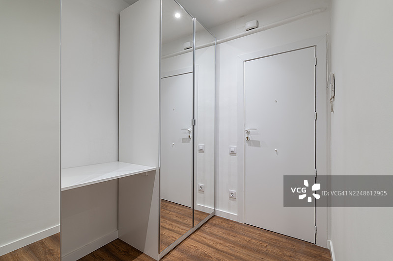 新公寓里，现代白色走廊铺设着木地板，并配有镜面衣柜图片素材