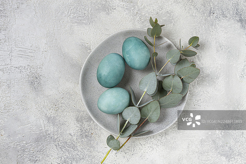 复活节彩蛋，以青绿色为主色调，放在灰色盘子上，旁边有一枝桉树枝，复活节贺卡，俯视视角，无人物图片素材