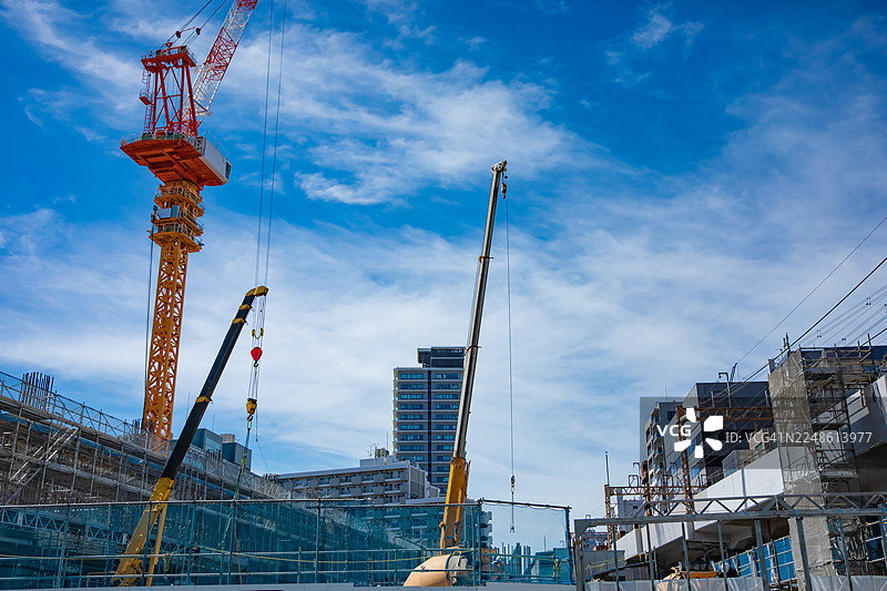 繁华建筑工地上，高耸的起重机在湛蓝的天空映衬下，低角度仰视图，象征着城市发展与进步图片素材