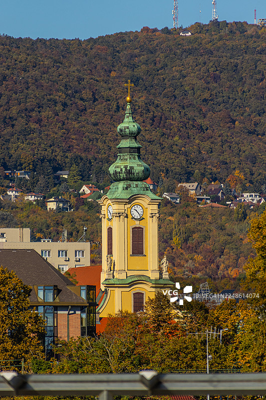 背景为秋季的山丘和住宅区，晴朗蓝天下历史悠久的教堂尖塔，匈牙利布达佩斯图片素材