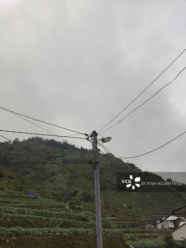 阴天下的印尼迭梦高原，电力塔和电线横跨山地农田景观图片素材