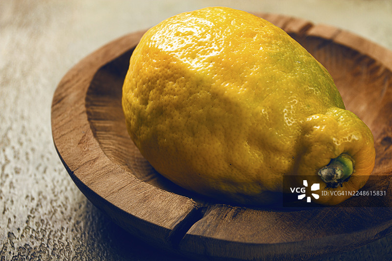 一个鲜活的柠檬摆放在古朴的木盘上，柔和的光线突显了它的质感和色彩，营造出温馨的家庭厨房氛围。图片素材