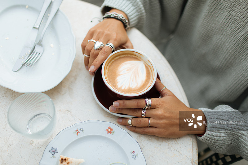 咖啡馆桌上，戴着银戒指的手，享受着拉花拿铁的惬意时光图片素材