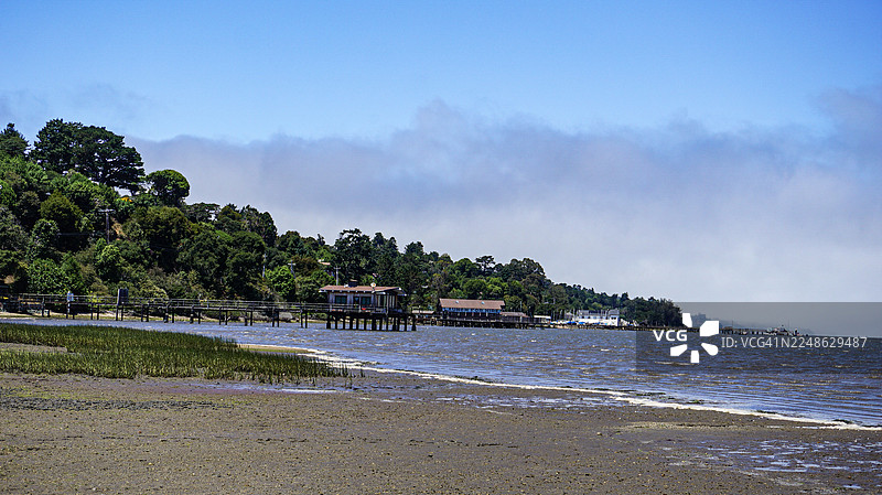 美国因弗内斯海滨小镇和海滩的风景，头顶阴云密布，特色是高跷建筑和郁郁葱葱的绿山，位于雷耶斯角国家海岸。图片素材