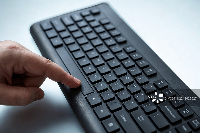 特写一只手在黑色电脑键盘上按键，展现现代科技与工作图片素材