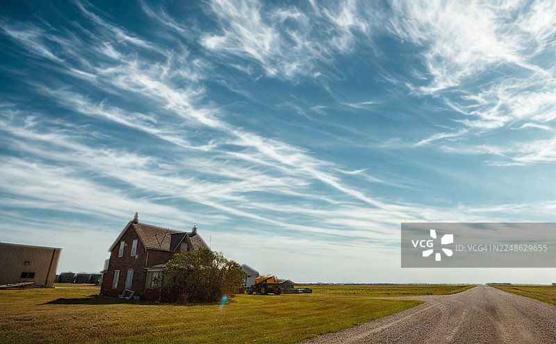 一栋古老的砖房坐落在乡村风景中，天空戏剧性地布满缕缕白云。图片素材