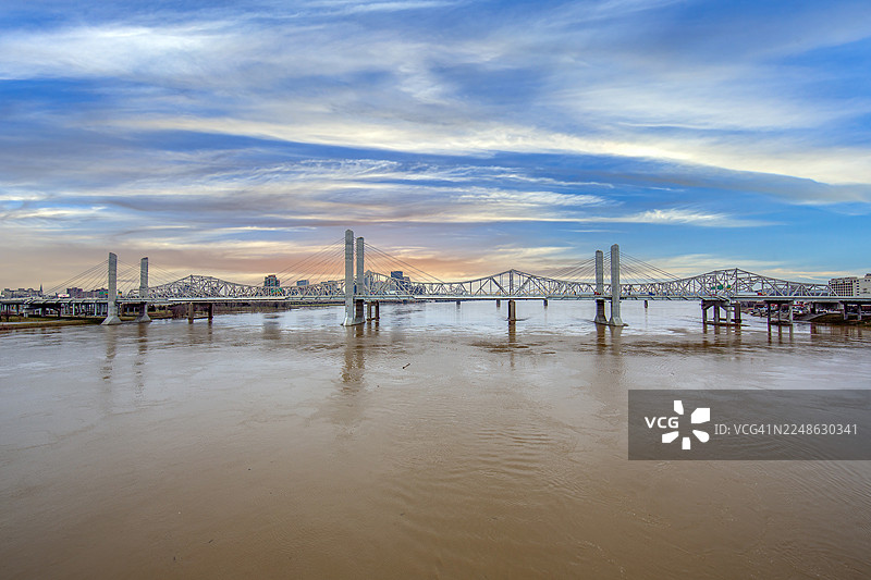 黄昏时分，现代桥梁横跨宽阔的河流，背景是戏剧性的多云天空，路易斯维尔，美国图片素材